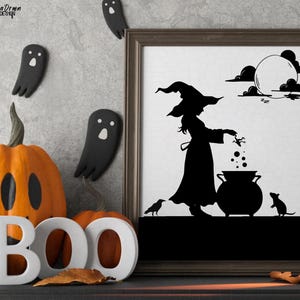May include: Halloween-themed decor featuring a framed silhouette art print of a witch, cauldron, and full moon. Orange pumpkin with a carved face and the word "BOO" in white letters. Black ghost and spider decorations complete the spooky scene.
