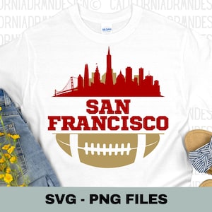 May include: White t-shirt with a red and gold design featuring the San Francisco skyline and a football. The text "SAN FRANCISCO" is written in red letters below the skyline.