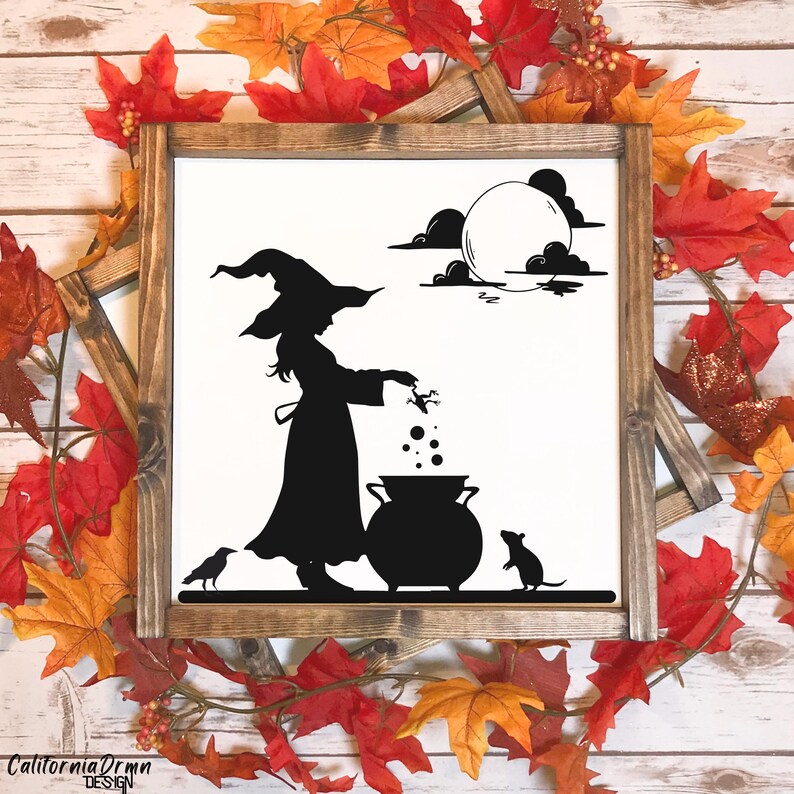 May include: A framed wooden sign with a black silhouette of a witch stirring a cauldron under a full moon. A crow and a mouse are also featured. The sign is surrounded by fall leaves. The text "California DrMn Design" is at the bottom.