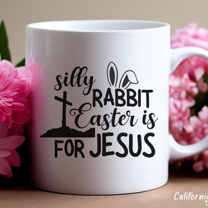 May include: White ceramic mug with a black design that says "silly rabbit easter is for jesus" with a cross and bunny ears.