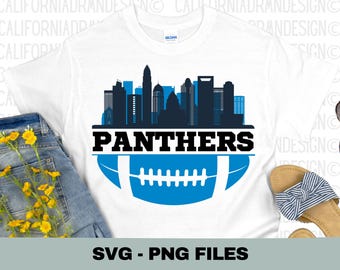 May include: A white t-shirt with a blue and black design of a football and a skyline with the word "PANTHERS" in black text.