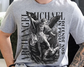 May include: Athletic heather gray t-shirt featuring a detailed graphic of Archangel Michael with a sword, defeating a demon. The text reads "Archangel Michael Defend Us". The shirt is a classic crew neck style.