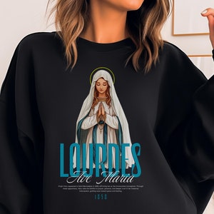 May include: Black sweatshirt with a blue and white graphic of the Virgin Mary, the words "Lourdes Ave Maria" and the year "1858".