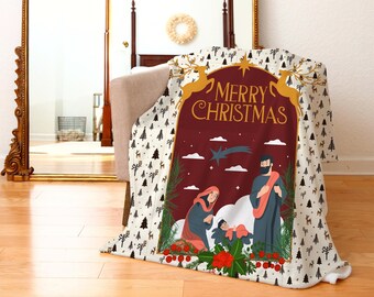 Pode incluir: Um cobertor branco e creme com uma cena de Natal vermelha e dourada. A cena apresenta uma cena de natividade com Maria, José e o menino Jesus. O texto "Merry Christmas" está escrito em letras douradas sobre um fundo vermelho.