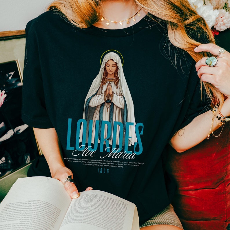 May include: Black t-shirt with a graphic of the Virgin Mary in blue and white, with the text "Lourdes Ave Maria 1858" underneath.