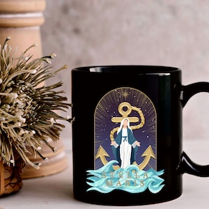 May include: Black ceramic mug featuring a graphic of a woman in a blue robe standing on a wave with an anchor and the text "Stella Maris".