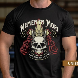 Pode incluir: Camiseta preta com uma caveira usando uma coroa e cercada por rosas. O texto "Memento Mori" est&aacute; acima da caveira e "Remember Your Death" est&aacute; abaixo. A palavra "UNISEX" est&aacute; no canto inferior direito.