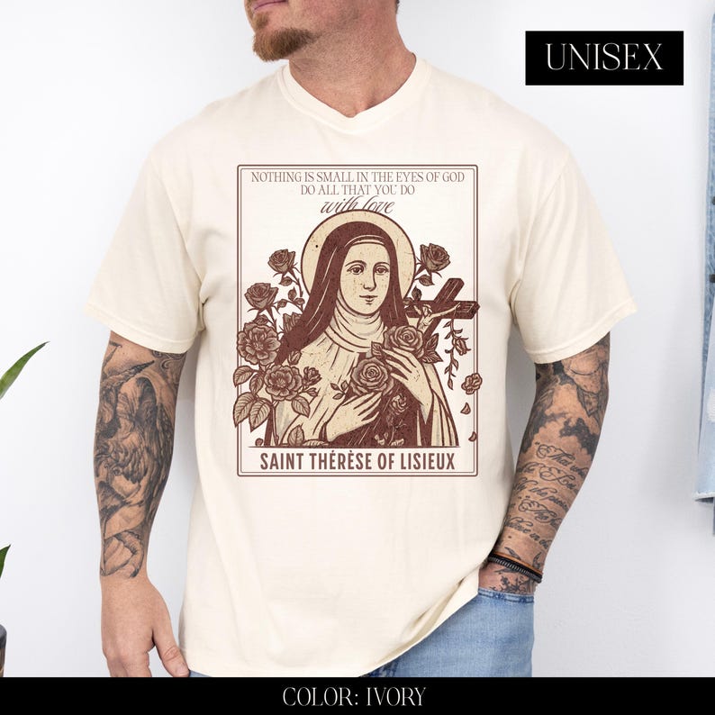 May include: Ivory unisex t-shirt featuring a graphic of Saint Th&eacute;r&egrave;se of Lisieux, roses, and the text "NOTHING IS SMALL IN THE EYES OF GOD DO ALL THAT YOU DO with love". The shirt is ivory in color.