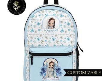 Puede incluir: Una mochila azul y blanca con un patrón floral. La mochila presenta un nombre personalizado, "MARIANNE", y una imagen de Nuestra Señora de Lourdes. La mochila es personalizable.