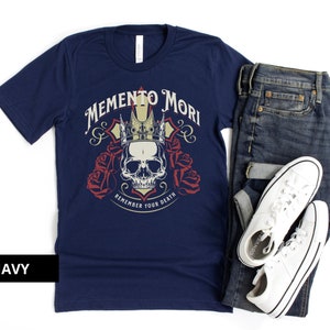 Pode incluir: Uma camiseta azul marinho com um gr&aacute;fico de caveira e coroa e o texto "Memento Mori Remember Your Death".