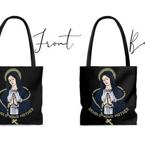 Op de afbeelding: Zwarte tote bag met een afbeelding van de Maagd Maria die bidt met een rozenkrans. De tekst "Behold Your Mother" is onder de afbeelding gedrukt.