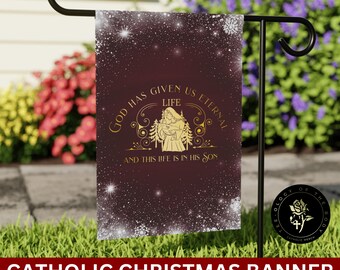 Può includere: Una bandiera da giardino color borgogna con un designo dorato. Il design presenta una donna che tiene un bambino, con il testo "Dio ci ha dato la vita eterna e questa vita è nel suo figlio". La bandiera ha un motivo a fiocco di neve bianco.