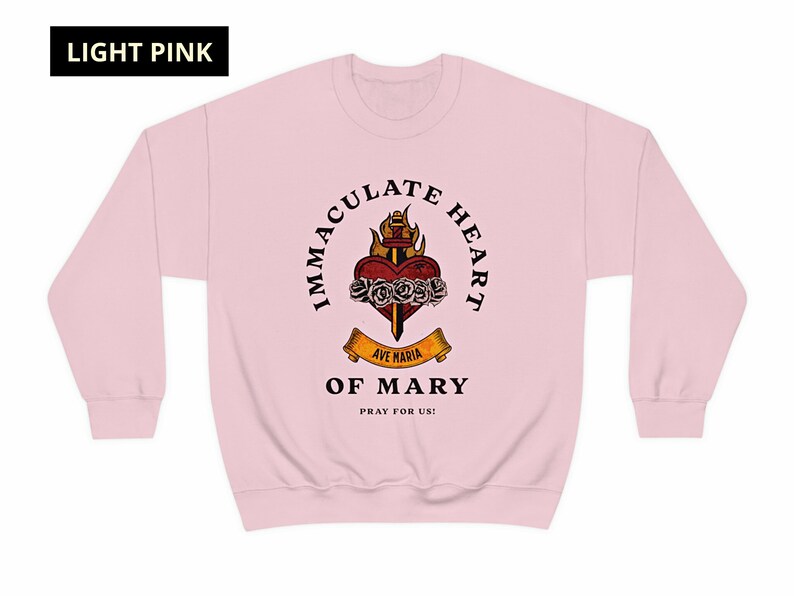 May include: A light pink sweatshirt with a graphic of the Immaculate Heart of Mary. The graphic features a heart with a sword, roses, and flames. The text "Immaculate Heart of Mary" is written in a circle around the graphic. The text "Ave Maria" is written on a banner below the graphic. The text "Pray for us!" is written below the banner.