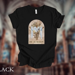May include: Black t-shirt with a graphic of a cross with a white cloth and green leaves in a brown arch. The text "HE IS RISEN" is below the graphic.