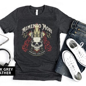 Pode incluir: Camiseta cinza escuro heather com um cr&acirc;nio usando uma coroa e as palavras "Memento Mori" e "Remember Your Death" impressas na frente.