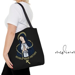 Op de afbeelding: Zwarte tote bag met een afbeelding van de Maagd Maria met een rozenkrans en de tekst "Behold Your Mother".