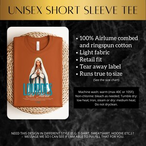 May include: A brown short-sleeved t-shirt with a graphic of the Virgin Mary and the text "Lourdes Ave Maria". The shirt is made of 100% airlume combed and ringspun cotton and has a retail fit.