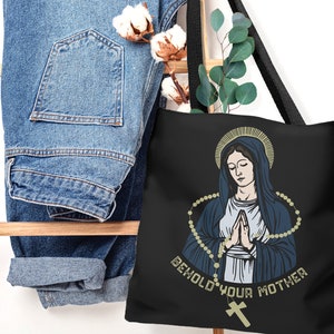 Op de afbeelding: Zwarte tote bag met een afbeelding van de Maagd Maria die een rozenkrans vasthoudt en de tekst "Behold Your Mother".