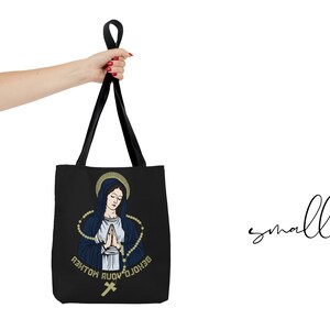 Op de afbeelding: Zwarte tote bag met een afbeelding van de Maagd Maria die bidt met een rozenkrans en de tekst "Zie, ik ben de dienstmaagd van de Heer".
