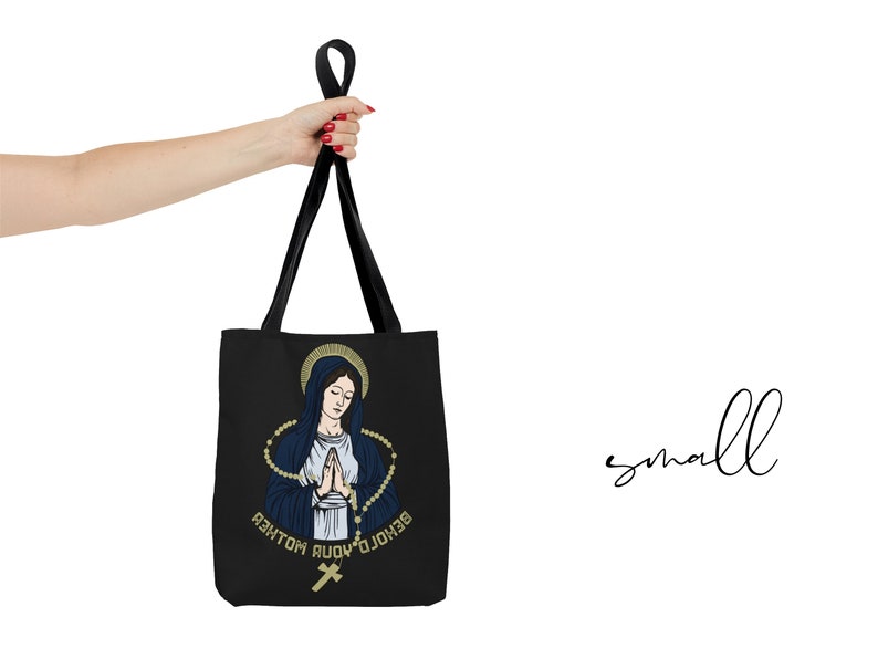 Op de afbeelding: Zwarte tote bag met een afbeelding van de Maagd Maria die bidt met een rozenkrans en de tekst "Zie, ik ben de dienstmaagd van de Heer".