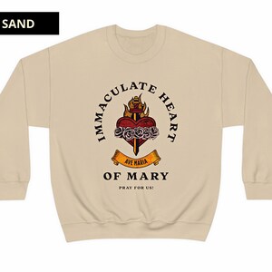 May include: A beige sweatshirt with a graphic print of a heart with a sword and flames. The text around the heart reads "Immaculate Heart of Mary" and "Ave Maria" with the words "Pray for Us!" below.