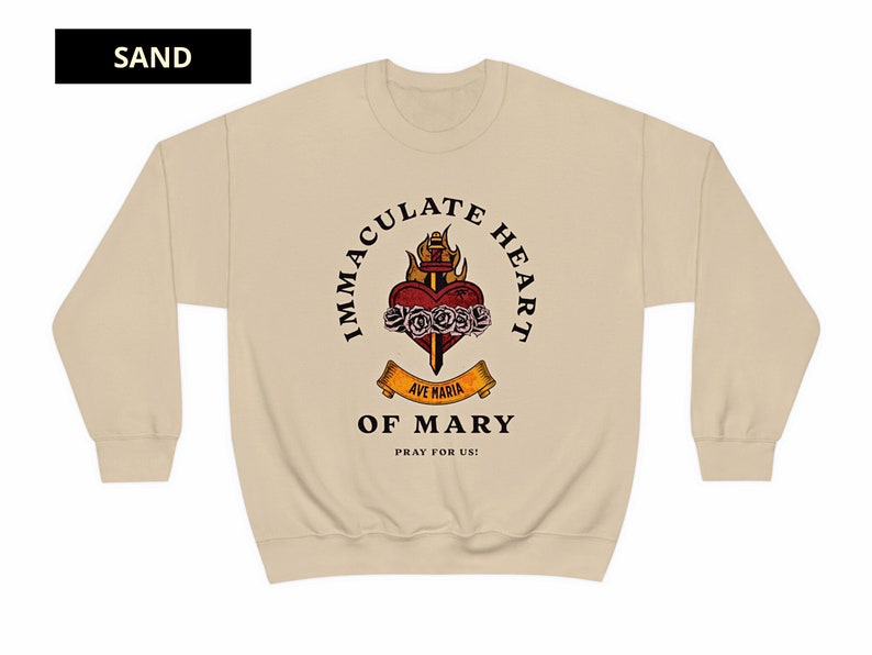 May include: A beige sweatshirt with a graphic print of a heart with a sword and flames. The text around the heart reads "Immaculate Heart of Mary" and "Ave Maria" with the words "Pray for Us!" below.