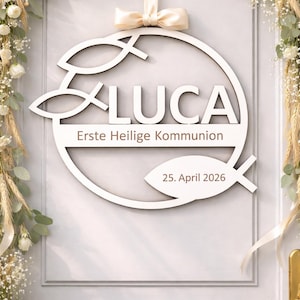 Könnte beinhalten: Weißes Holzschild mit dem Namen "LUCA" und dem Text "Erste Heilige Kommunion" und "25. April 2026". Das Schild ist mit Fischsymbolen und einer cremefarbenen Schleife verziert. Der Hintergrund ist eine weiße Tür mit Blumengestecken.