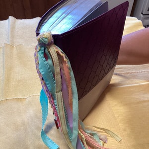 May include: A purple leather-bound book with a decorative bookmark made of colourful ribbons.