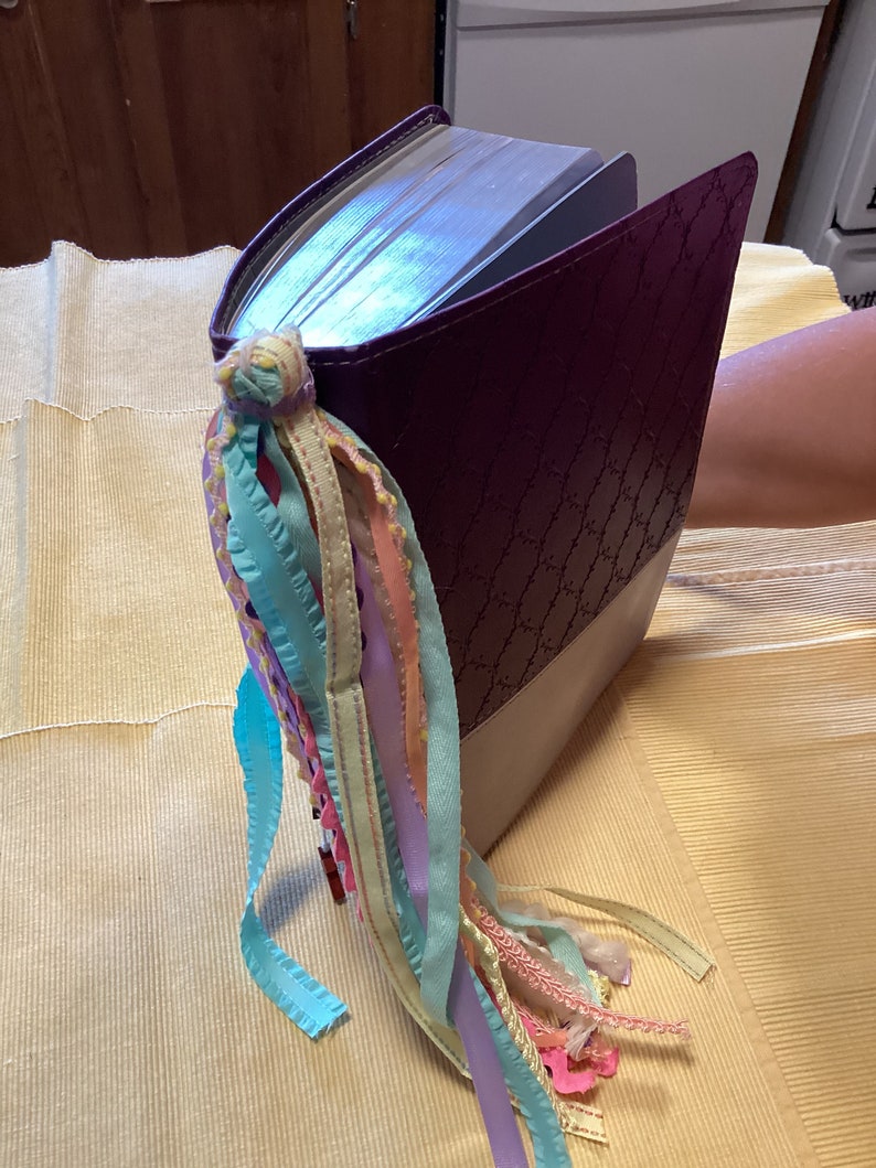 May include: A purple leather-bound book with a decorative bookmark made of colourful ribbons.