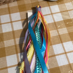 May include: A colourful assortment of ribbons and trims tied together in a bundle. The ribbons are in shades of blue, green, yellow, pink, and purple.