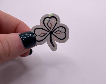 May include: A black and white shamrock sticker with a glittery iridescent finish. The shamrock is a traditional Irish symbol.