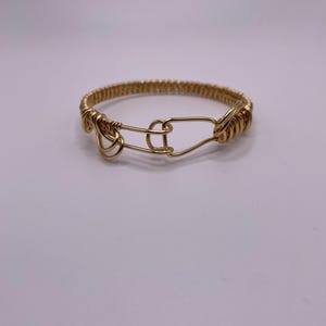 May include: A gold wire bracelet with a clasp closure. The bracelet is made of multiple strands of wire that are twisted together.