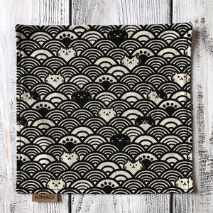Könnte beinhalten: Ein quadratisches Stofftuch mit einem sich wiederholenden Muster aus schwarzen und cremefarbenen konzentrischen Halbkreisen, durchsetzt mit kleinen Katzengesichtern und Pfotenabdrücken. Unten ist ein kleines braunes Etikett mit KIMACI angebracht.