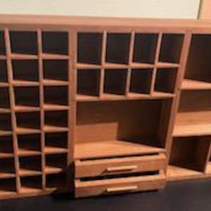 Puede incluir: Un organizador de madera de color marr&oacute;n claro que presenta una rejilla de peque&ntilde;os compartimentos cuadrados a la izquierda, una secci&oacute;n con cub&iacute;culos cuadrados de tama&ntilde;o mediano en el centro, dos cajones horizontales y estantes abiertos a la derecha.