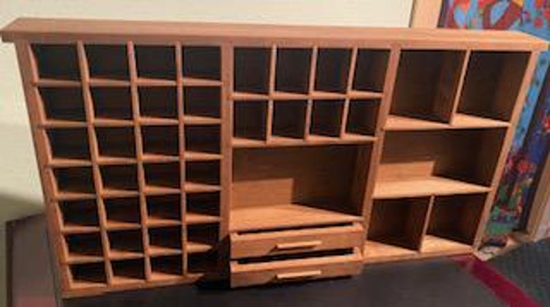 Puede incluir: Un organizador de madera de color marr&oacute;n claro que presenta una rejilla de peque&ntilde;os compartimentos cuadrados a la izquierda, una secci&oacute;n con cub&iacute;culos cuadrados de tama&ntilde;o mediano en el centro, dos cajones horizontales y estantes abiertos a la derecha.