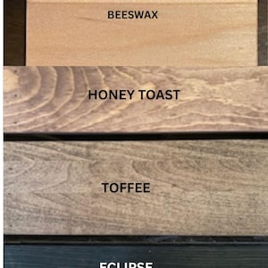 May include: Four rectangular wooden planks arranged vertically, each displaying a distinct wood stain color. The labels BEESWAX, HONEY TOAST, TOFFEE, and ECLIPSE are printed in black text on the corresponding light, medium, and dark wood surfaces.
