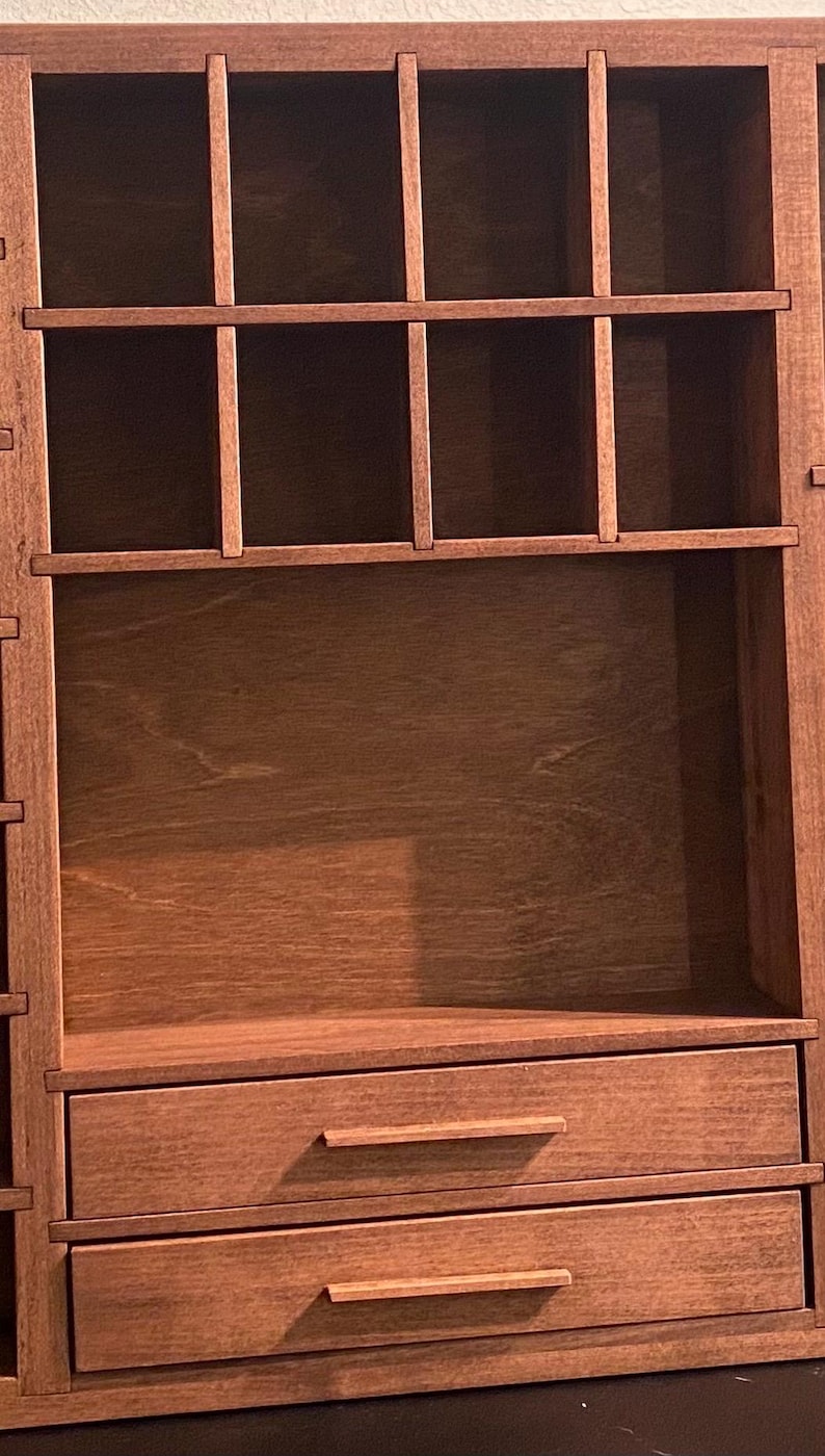 Puede incluir: Un organizador de pared de madera marr&oacute;n que presenta una secci&oacute;n superior con cuatro compartimentos rectangulares abiertos y una secci&oacute;n inferior que contiene dos cajones horizontales, cada uno con un tirador de madera fino.