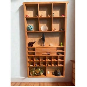 May include: A tall, light-toned wooden wall shelf featuring multiple rectangular cubbies of varying sizes, two central drawers with horizontal handles, and an open design filled with assorted small decorative objects, crystals, and figurines.