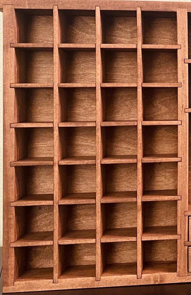Puede incluir: Una vitrina rectangular de madera que presenta una cuadr&iacute;cula de m&uacute;ltiples compartimentos cuadrados. La unidad est&aacute; construida con madera de tono marr&oacute;n medio con una veta visible, organizada en cuatro columnas verticales y siete filas horizontales.