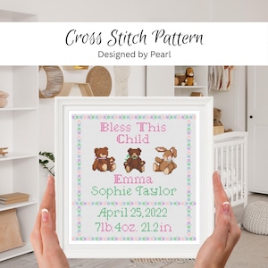 May include: A framed cross stitch pattern featuring the text Bless This Child, the name Emma Sophie Taylor, and the birth details April 25, 2022, 7lb 4oz, 21.2in. The design includes three brown stuffed animals and a pastel checkered border.