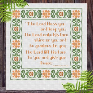 Peut inclure: Un motif de point de croix sur tissu blanc avec une citation en orange tirée de Nombres 6:24-26, encadrée par une bordure florale répétitive verte et orange. Le texte indique : The Lord bless you and keep you, the Lord make his face shine.
