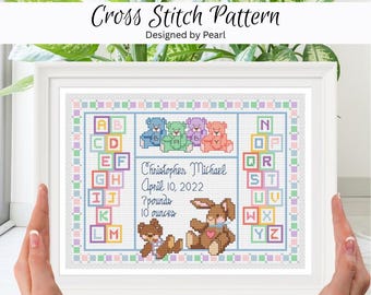 Peut inclure: Un modèle de point de croix encadré avec le texte Christopher Michael, April 10, 2022, 7 pounds, 10 ounces, des blocs alphabétiques colorés, quatre petits ours en peluche pastel, un ours brun et un lapin brun avec un cœur rose.