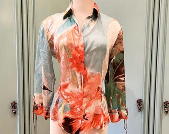 May include: A long-sleeved button-up shirt with a floral print in shades of pink, orange, green, and blue. The shirt has a fitted silhouette and a tie detail at the cuffs.