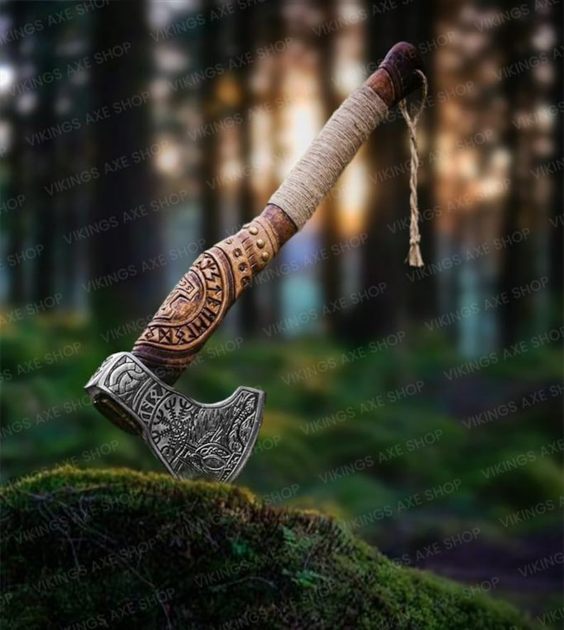 May include: A hand-crafted Viking axe with a wooden handle and a metal head. The handle is decorated with intricate carvings and the head features a detailed design of a wolf's head. The axe is resting on a bed of moss.
