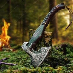 May include: A detailed image of a Viking axe with a wooden handle wrapped in dark brown leather. The axe head is silver with intricate carvings. The axe is resting on a mossy tree stump in a forest setting, with a blurred background and a small fire.