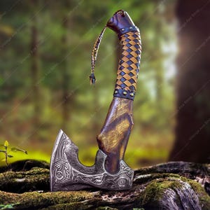May include: A hand-forged Viking axe with a brown wooden handle wrapped in a braided leather strap. The axe head has intricate carvings and a sharp blade.