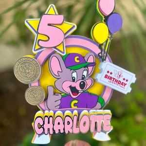 Op de afbeelding: Kleurrijke taarttopper met een cartoon muis die een duim omhoog geeft. De topper bevat het nummer 5 in een ster, ballonnen en de naam "CHARLOTTE". Bevat ook de tekst "BIRTHDAY celebrations".