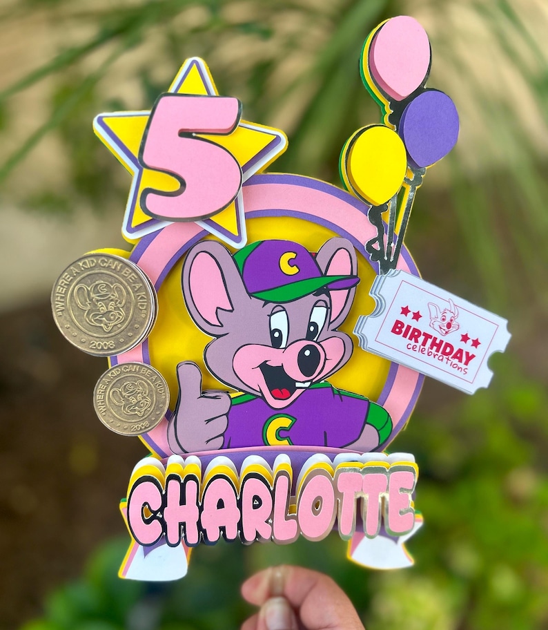 Op de afbeelding: Kleurrijke taarttopper met een cartoon muis die een duim omhoog geeft. De topper bevat het nummer 5 in een ster, ballonnen en de naam "CHARLOTTE". Bevat ook de tekst "BIRTHDAY celebrations".