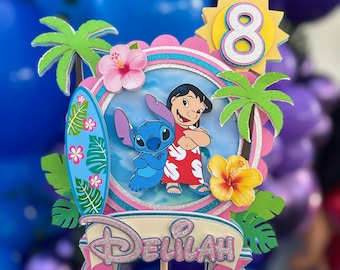 May include: A pink and blue cake topper with a cartoon image of Stitch and Lilo from the Disney movie Lilo & Stitch. The topper also features a yellow sun with the number 8 and the name "Delilah" in pink glitter letters.