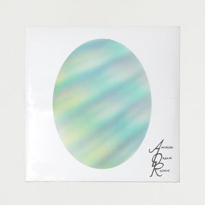 May include: A white square box with a holographic, iridescent, oval sticker in the center. The sticker has a blue, green, and yellow color scheme. The text "America Dream Reserve" is printed in black on the bottom right corner of the box.